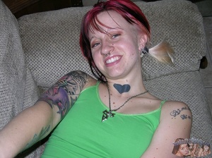 Young babe with red hair and tattoos lays down on a gray couch then pulls down her jeans and blue panty and reveals her alluring pussy before she takes off her green shirt and shows her tiny tits as she lays down naked on a gray bed. - Picture 1