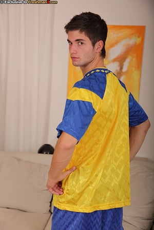 Gorgeous soccer player in blue and gold uniform takes off his shirt and shows his muscular body before he pulls down his shorts and black brief and reveals his large dick as he sits on a white couch. - Picture 3