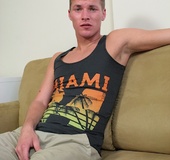 Sexy man sits on a brown couch then removes his black Miami shirt before