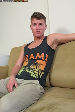 Sexy man sits on a brown couch then removes his black Miami shirt before he peels down his gray pants and white brief and wanks his big cock. - Picture 2