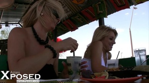 Two lusty blondes in white shirt and jeans skirt and in black dress reveals their lusty twat under their table as they spread their legs wide on a green bench in an outdoor fast food. - Picture 12