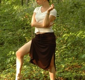 Girl with a bun and a thin white top smokes in the woods