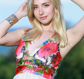 Blonde girl takes off floral sun dress by the lake, poses seductively.