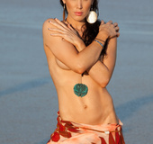 Sexy black haired babe wearing a necklace has fun undressing on the sand