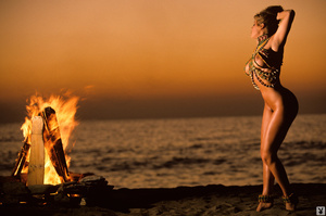 Seductive babe in beaded long necklace across her large fake breasts by warm beach bon fire - Picture 3