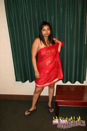 Dark haired indian in red saree undressing on a cam and exposing her big boobies while posing on the table - Picture 1