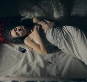 Brown haired babe in long flowing dress rests peacefully on a large bed