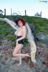This classy, redheaded slut, wearing black and pearls, poses outside on