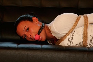 Pretty brunette in jeans and white top ball gagged and hog tied with ropes on sofa - Picture 4