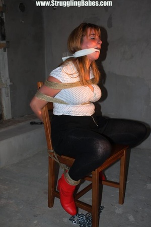Busty brunette in white top and black pants roped tight to chair and gagged - Picture 6