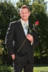 Grey eyed bloke in dark suit and grey tie posing outdoors with red rose