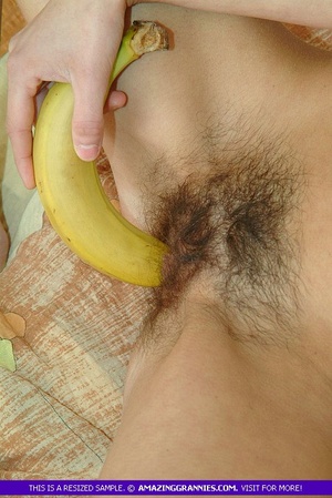 Skinny granny shows her petite tits as she lays naked on a brown and green bed while she shoves a big banana deep in her twat. - Picture 2