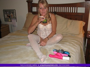 Hot granny pose her fat body in white nighty and stockings then shows her small boobs while she drills and rubs her crack with different toys on a white bed. - Picture 2