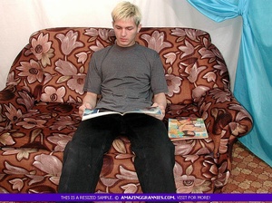Fat granny wearing white blouse and green dress sits on a brown couch and jacks a young blonde's dick. - Picture 1