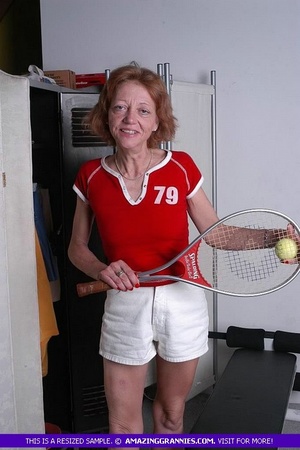 Luscious granny pose her old body while holding a tennis racket before she expose her small tits wearing her red shirt and white shorts. - Picture 1