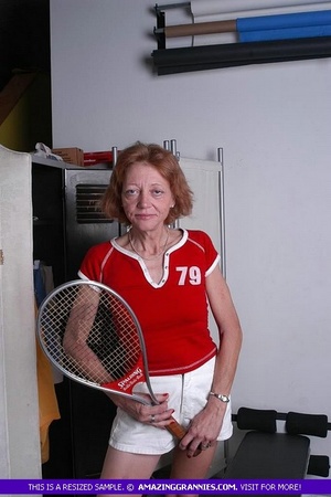 Luscious granny pose her old body while holding a tennis racket before she expose her small tits wearing her red shirt and white shorts. - Picture 3