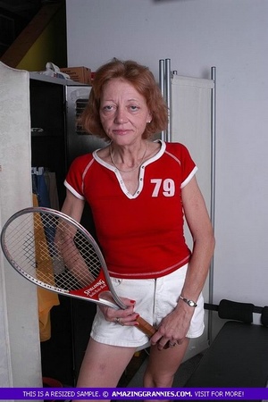Luscious granny pose her old body while holding a tennis racket before she expose her small tits wearing her red shirt and white shorts. - Picture 4