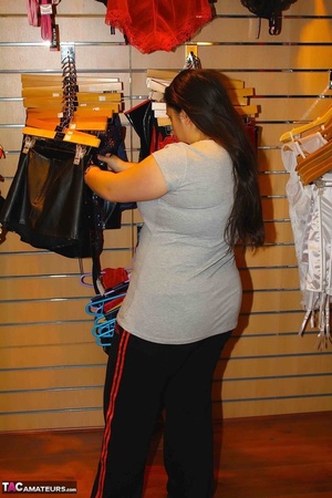 [Cute babe pose her chubby body in gray shirt, black jogging pants and boots in a sex shop before she gets naked and puts on her violet and black nighty, black stockings and high heels in a fitting room. - XXXonXXX - Pic 3