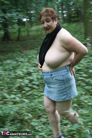Chubby granny pose in the woods then peels off her black shirt and releases her giant tits before she pulls down her jeans skirt and teases with her humongous ass then pulls down her blue panty and expose her lusty pussy wearing her blue high heels. - Picture 3
