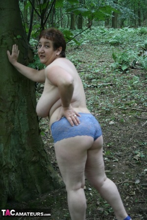 Chubby granny pose in the woods then peels off her black shirt and releases her giant tits before she pulls down her jeans skirt and teases with her humongous ass then pulls down her blue panty and expose her lusty pussy wearing her blue high heels. - Picture 15