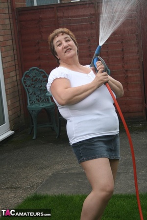 Plus size granny gets her big body wet with a hose on her lawn before she pulls down her jeans skirt and expose her lusty pussy then lifts up her white shirt and expose her humongous juggs. - Picture 2