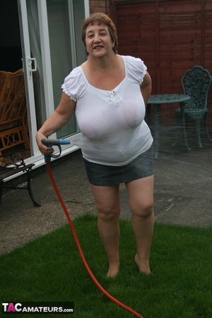 Plus size granny gets her big body wet with a hose on her lawn before she pulls down her jeans skirt and expose her lusty pussy then lifts up her white shirt and expose her humongous juggs. - Picture 5