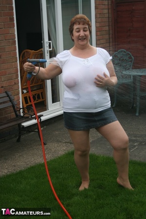 Plus size granny gets her big body wet with a hose on her lawn before she pulls down her jeans skirt and expose her lusty pussy then lifts up her white shirt and expose her humongous juggs. - Picture 7