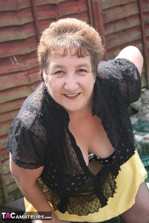 Steaming hot granny peels off her black blouse and yellow skirt and displays her chubby body in multi, colored underwear, black stockings and yellow high heels outdoor. - XXXonXXX - Pic 3