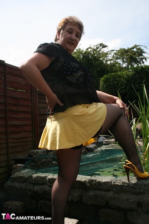 Steaming hot granny peels off her black blouse and yellow skirt and displays her chubby body in multi, colored underwear, black stockings and yellow high heels outdoor. - XXXonXXX - Pic 5