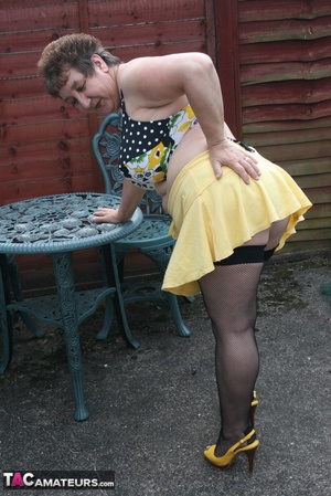 Steaming hot granny peels off her black blouse and yellow skirt and displays her chubby body in multi, colored underwear, black stockings and yellow high heels outdoor. - Picture 10