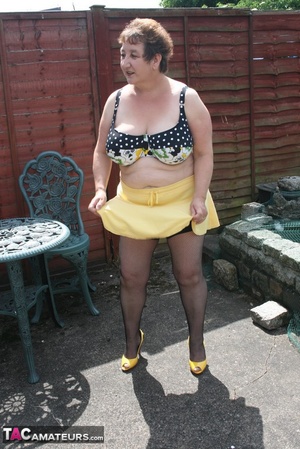 Steaming hot granny peels off her black blouse and yellow skirt and displays her chubby body in multi, colored underwear, black stockings and yellow high heels outdoor. - Picture 12