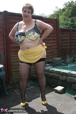 Steaming hot granny peels off her black blouse and yellow skirt and displays her chubby body in multi, colored underwear, black stockings and yellow high heels outdoor. - Picture 13