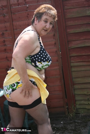 Steaming hot granny peels off her black blouse and yellow skirt and displays her chubby body in multi, colored underwear, black stockings and yellow high heels outdoor. - Picture 16
