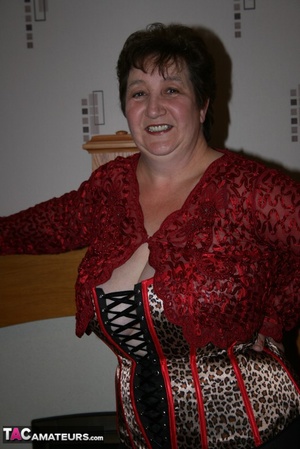 Chubby granny takes off her red blouse and displays her big body before she takes off her multi colored leopard print corset and expose her large breasts in different poses wearing her black leggings and brown and black high heels on the floor. - Picture 1