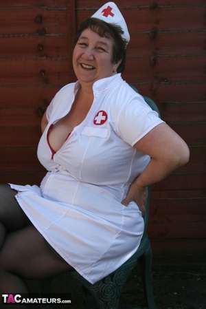 Nurse granny peels off her white uniform and teases with her large body then shows her giant breasts wearing her black lingerie, stockings and white high heels outdoor. - XXXonXXX - Pic 1