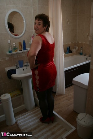 Alluring granny peels off her red dress and seduces with her plus size body in red and black lingerie, black stockings and red high heels in different poses in the bathroom. - Picture 2