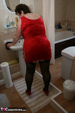 Alluring granny peels off her red dress and seduces with her plus size body in red and black lingerie, black stockings and red high heels in different poses in the bathroom. - Picture 3