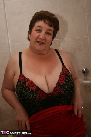 Alluring granny peels off her red dress and seduces with her plus size body in red and black lingerie, black stockings and red high heels in different poses in the bathroom. - Picture 17