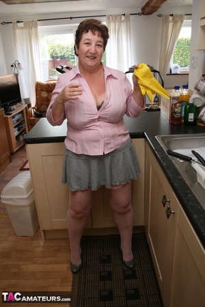Mature plomper displays her chubby body in pink shirt, gray skirt, underwear, pink stockings and gray high heels in different poses in her kitchen. - Picture 8