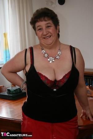 Mature plomper peels off her black shirt and red leather skirt and pose her chubby body in red and black lingerie, black stockings and high heels on a brown table. - XXXonXXX - Pic 1