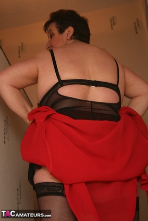 Chubby granny takes off her red robe and displays her her plus size body in red and black lingerie, black stockings and red high heels in different poses before she reveals her monster breasts on a green stairway. - Picture 9