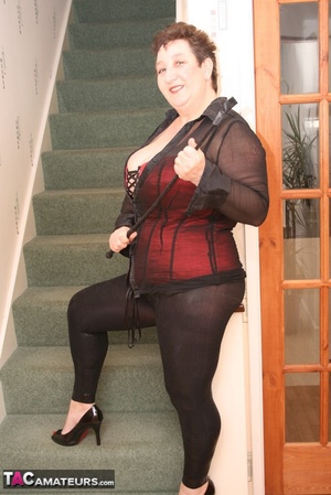 Cute granny peels off her black see through blouse and teases with her plus size body in different poses on a green stairway wearing her red and black corset, black leggings and high heels. - XXXonXXX - Pic 1