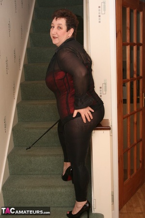Cute granny peels off her black see through blouse and teases with her plus size body in different poses on a green stairway wearing her red and black corset, black leggings and high heels. - Picture 2