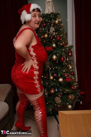 Mature plomper displays her large body in red santa hat, dress, panty and boots on a gray and brown couch before she reveals her monster boobs and juicy pussy in different poses. - Picture 4