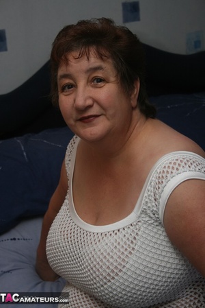 Naughty granny displays her plus size body before she expose her humongous tits in different poses wearing her white dress, lingerie and boots on a blue bed. - Picture 1