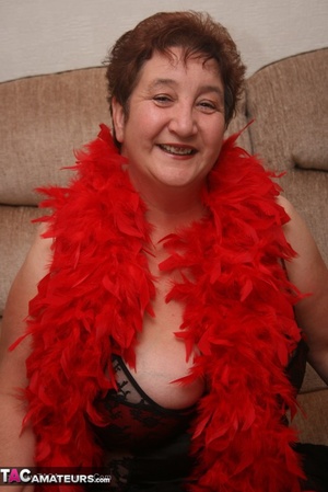 Mature plomper in red and black lingerie, red fur scarf, stockings and black high heels pulls down her nighty and reveals her humongous boobs in different poses on a brown couch. - XXXonXXX - Pic 2