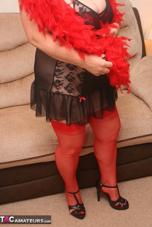 Mature plomper in red and black lingerie, red fur scarf, stockings and black high heels pulls down her nighty and reveals her humongous boobs in different poses on a brown couch. - XXXonXXX - Pic 4