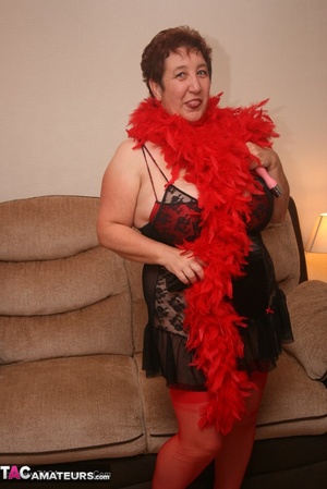 Mature plomper in red and black lingerie, red fur scarf, stockings and black high heels pulls down her nighty and reveals her humongous boobs in different poses on a brown couch. - XXXonXXX - Pic 5