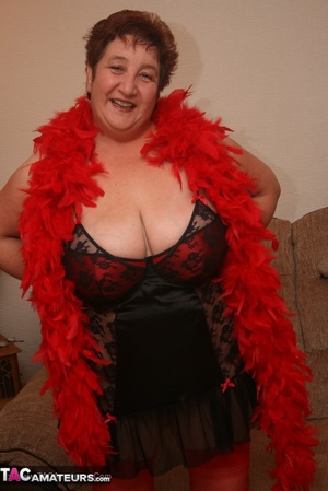 Mature plomper in red and black lingerie, red fur scarf, stockings and black high heels pulls down her nighty and reveals her humongous boobs in different poses on a brown couch. - XXXonXXX - Pic 6