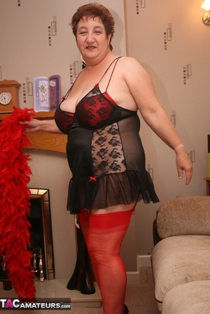 Mature plomper in red and black lingerie, red fur scarf, stockings and black high heels pulls down her nighty and reveals her humongous boobs in different poses on a brown couch. - XXXonXXX - Pic 13
